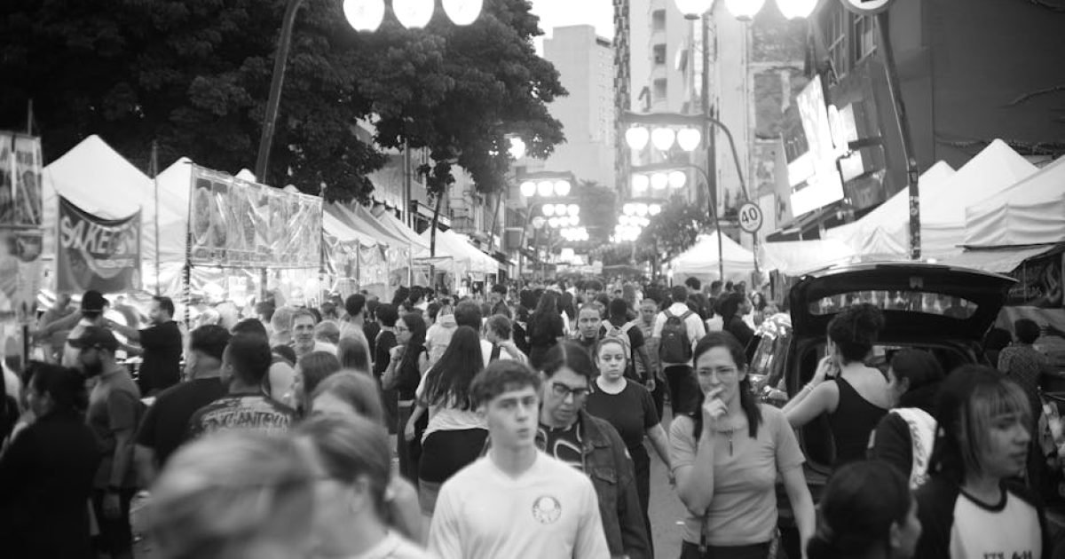 Mercado de rua movimentado com público diversificado em preto e branco.