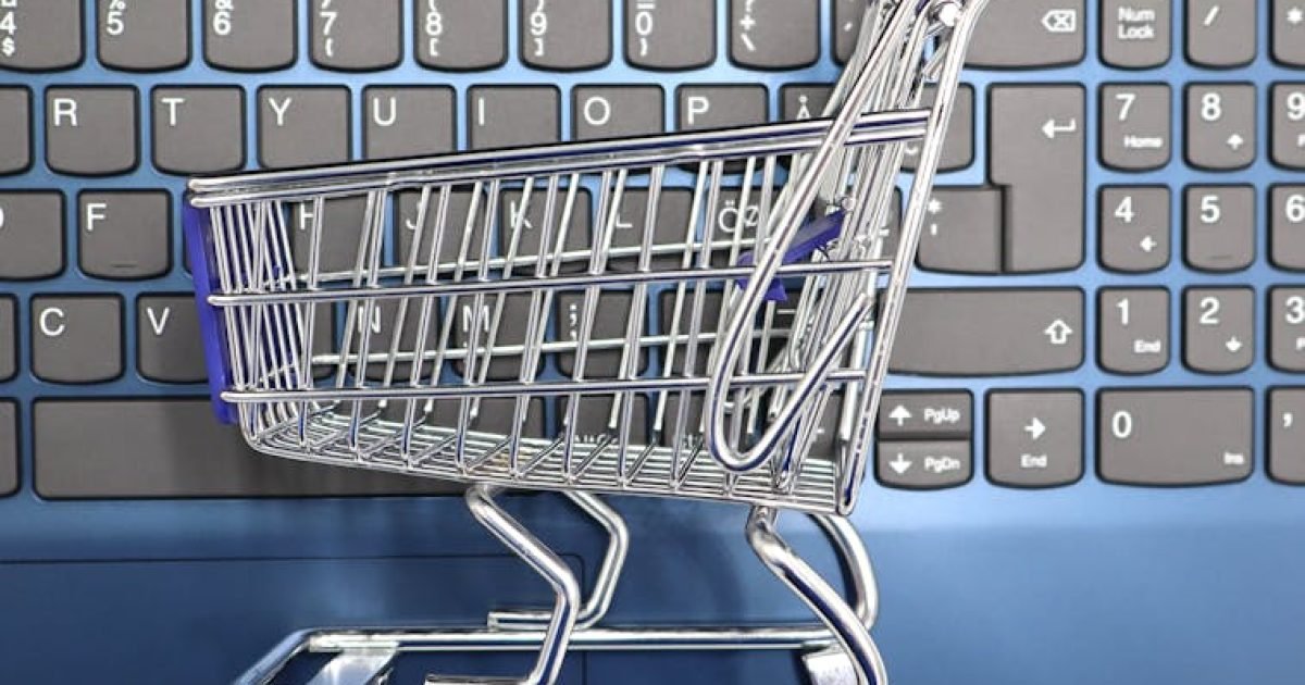 Um carrinho de compras em miniatura colocado sobre o teclado de um laptop simboliza as compras online e o comércio eletrônico.