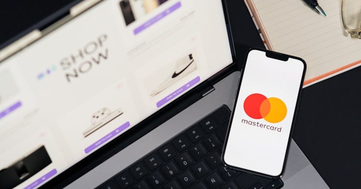 Laptop e smartphone com logotipo da Mastercard, ilustrando compras on-line e pagamentos digitais.